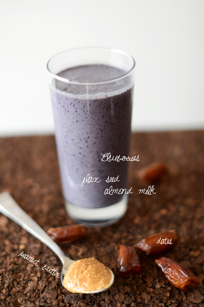 A tall glass of our Peanut Butter and Jelly Date Smoothie Recipe surrounded by ingredients used to make it