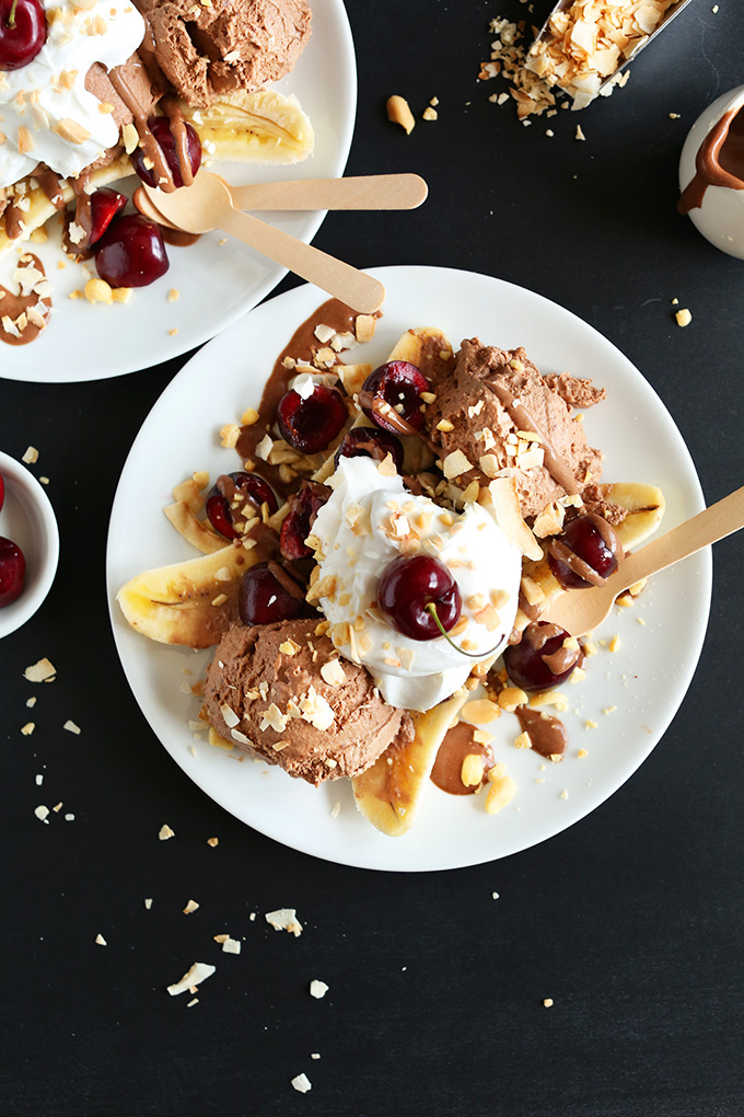 Plates loaded with Vegan Banana Splits made with chocolate ice cream, coconut whip, peanuts, and cherries