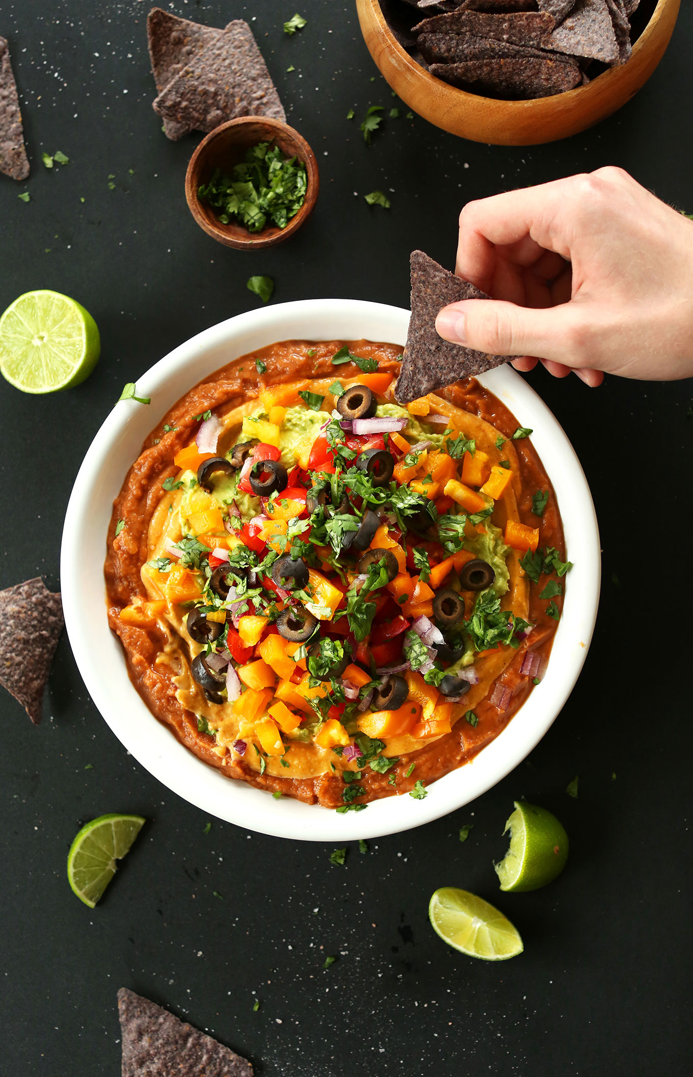 Dipping a blue corn tortilla chip into a bowl of our 7-Layer Mexican Dip recipe