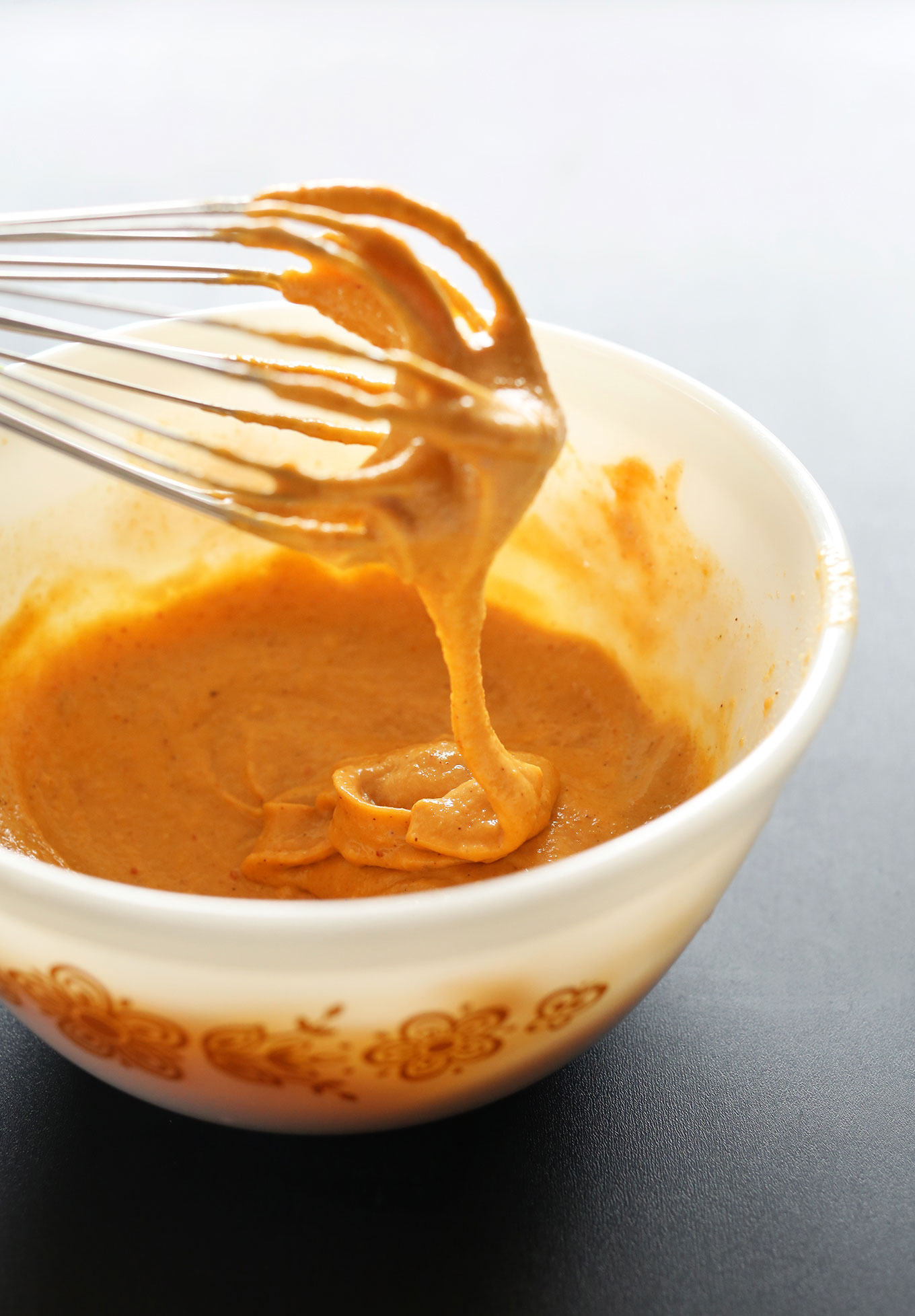 Vegan Mexican Queso falling off a whisk into a bowl