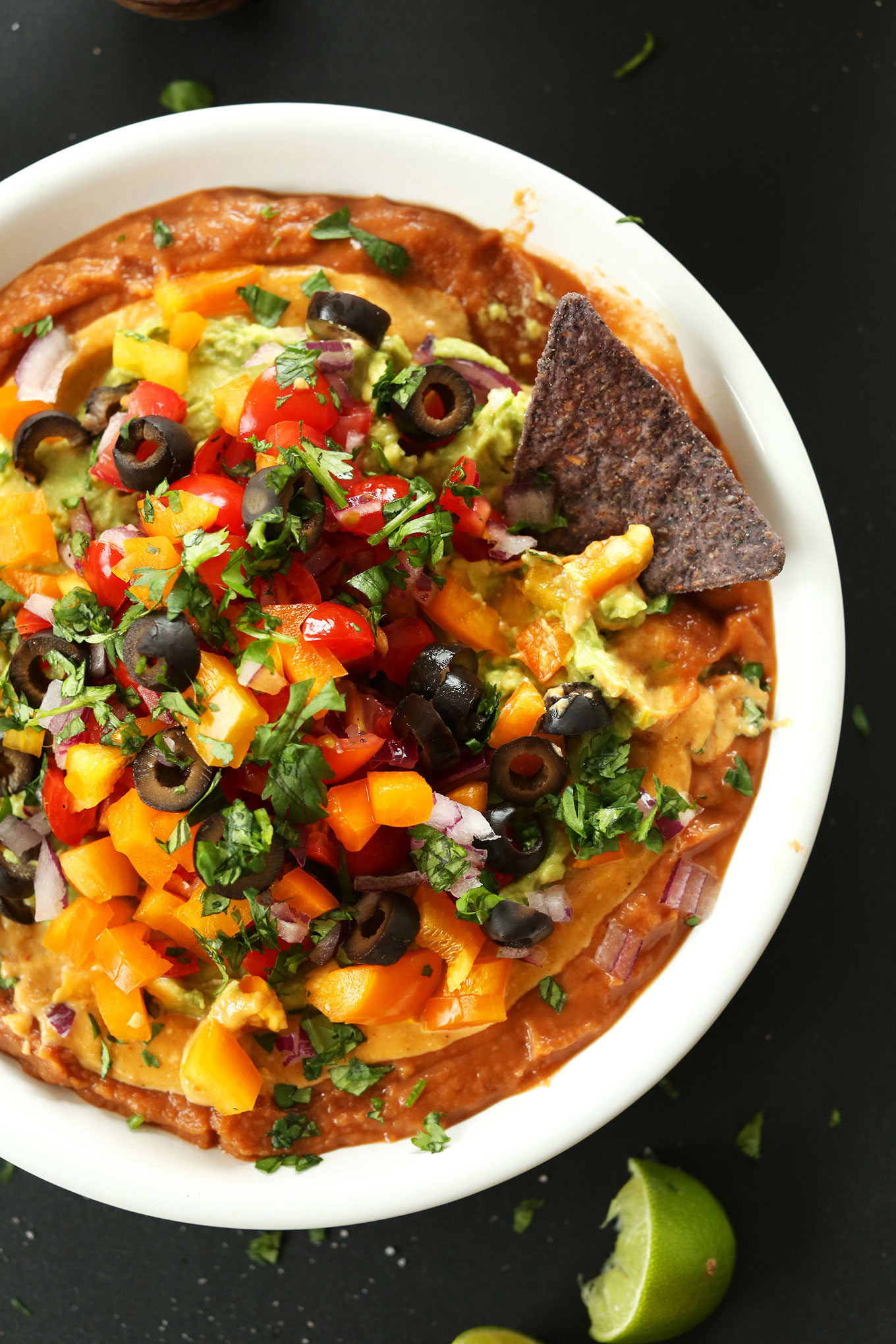 Blue corn tortilla chip in a big bowl of our homemade Vegan 7-Layer Mexican Dip