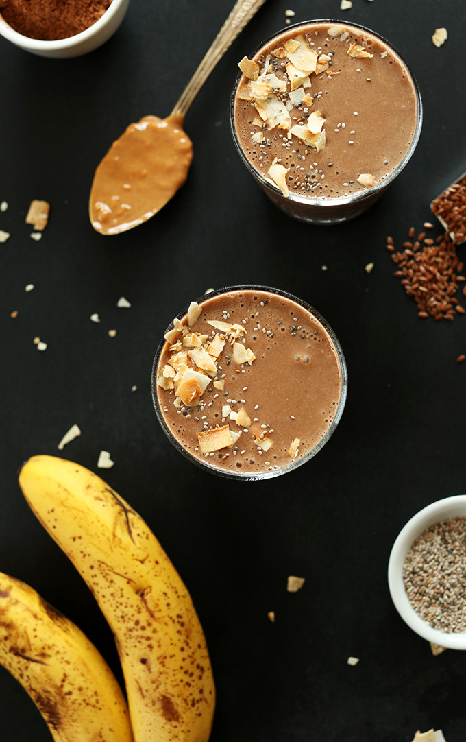 Glasses of vegan Chocolate Chia Recovery Drink surrounded by ingredients used to make it