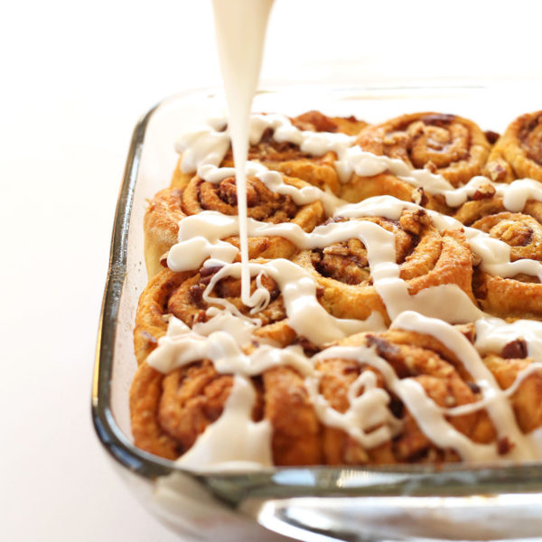 Drizzling glaze over a batch of Vegan Pumpkin Cinnamon Rolls