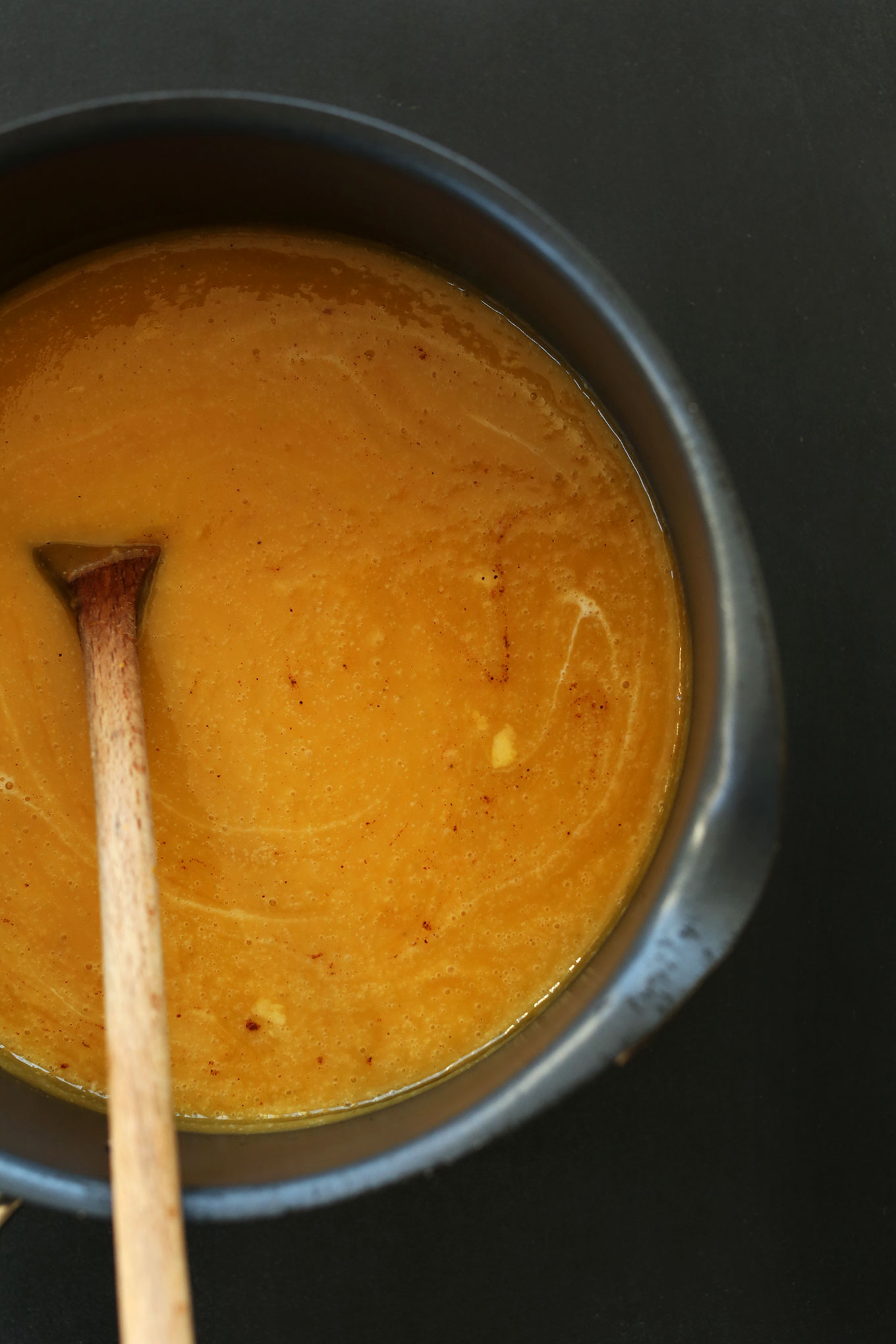 Using a wooden spoon to stir a pot of our Savory Pumpkin Soup recipe