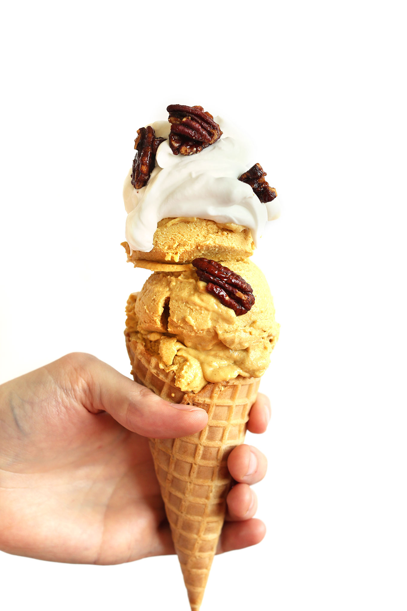 Holding up a cone filled with Vegan Pumpkin Pie Ice Cream topped with coconut whip and glazed pecans