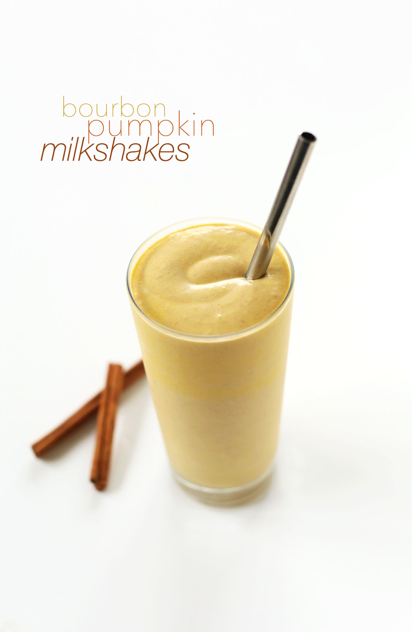 Tall glass of our creamy vegan Bourbon Pumpkin Milkshake with cinnamon sticks and a straw