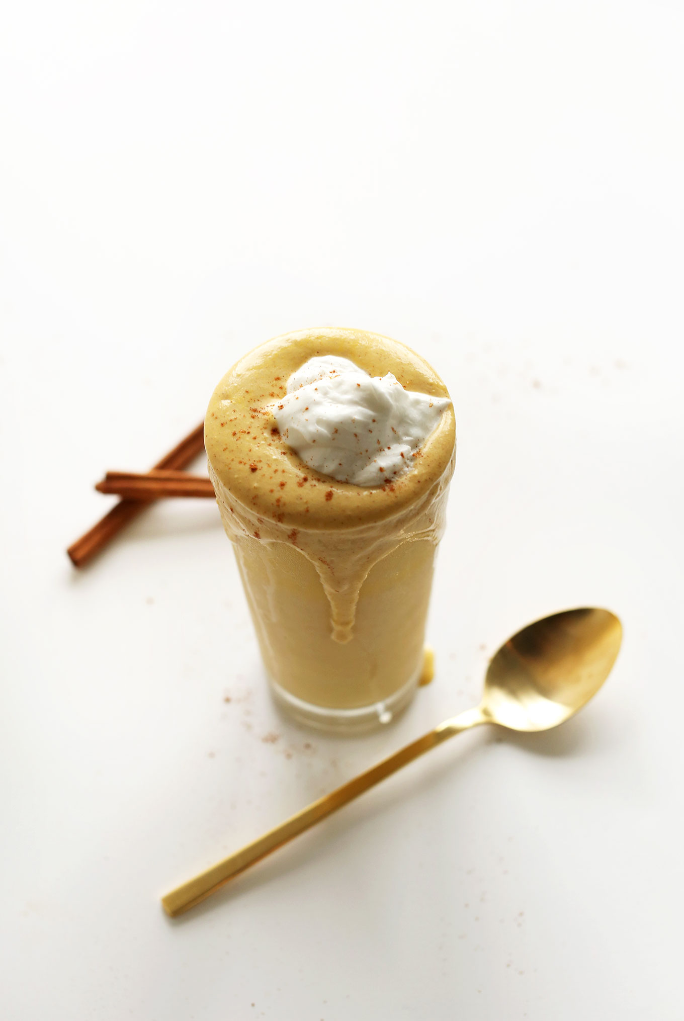 Overflowing glass of Boozy Pumpkin Milkshake topped with coconut whip