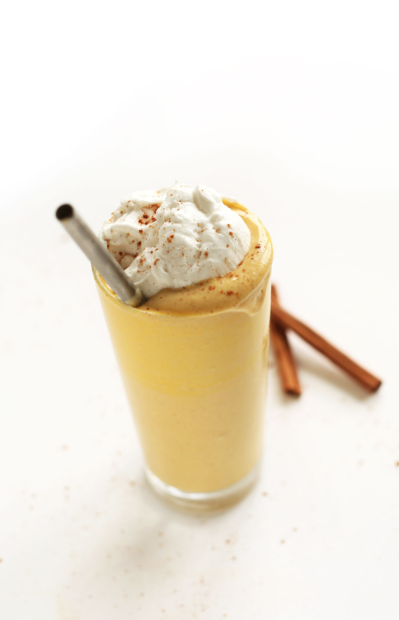 Tall glass of Boozy Pumpkin Milkshake topped with coconut whip and a dash of cinnamon