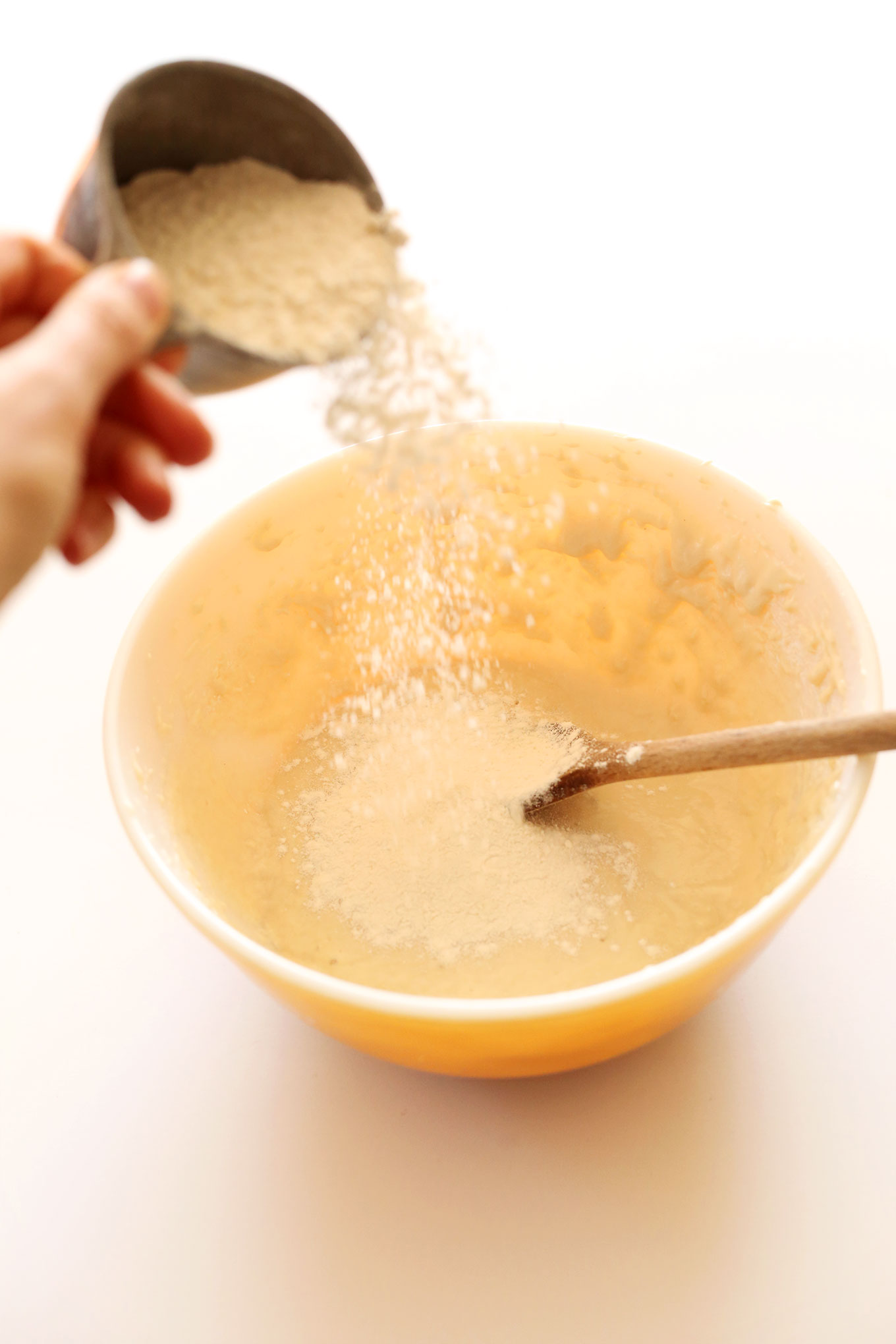 Pouring flour into batter for our vegan dinner rolls recipe