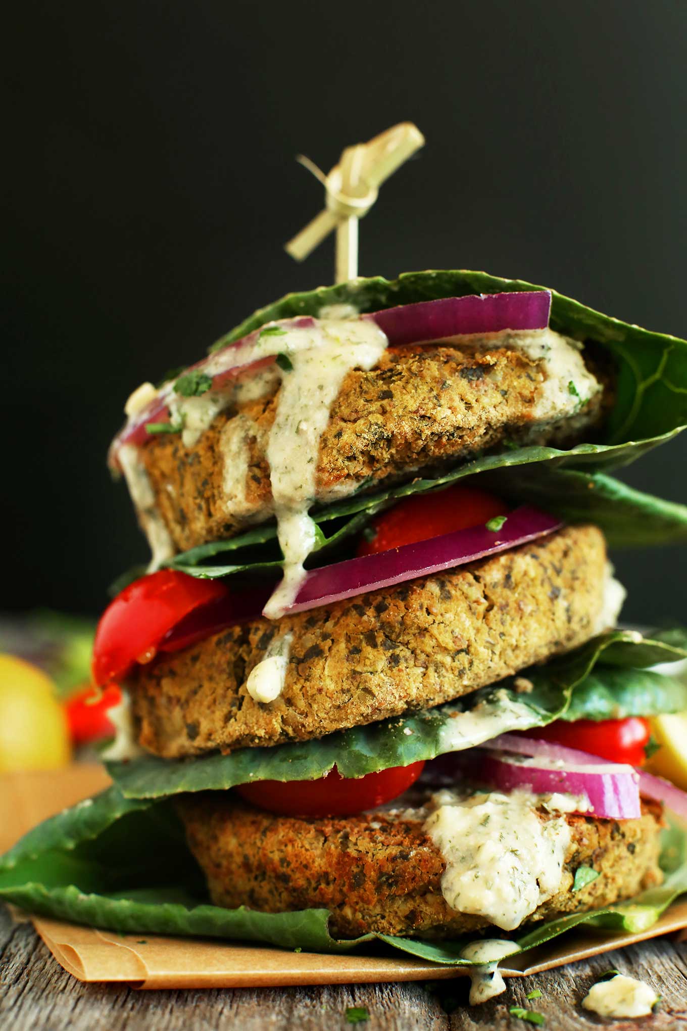 Stacked falafel burgers in collard green wraps with onion, tomato, and sauce