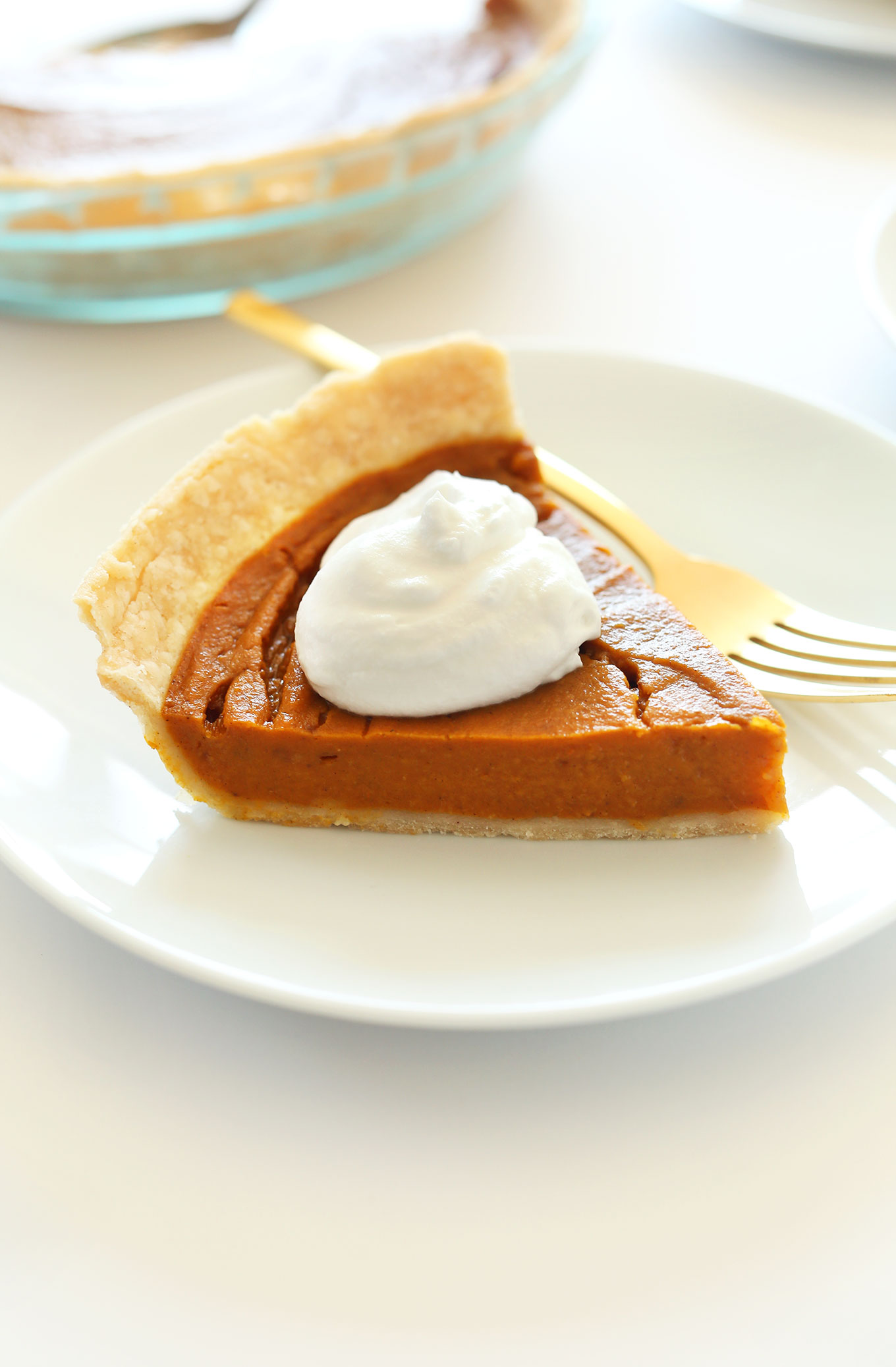 Small plate with a slice of Vegan Gluten-Free Pumpkin Pie topped with coconut whipped cream