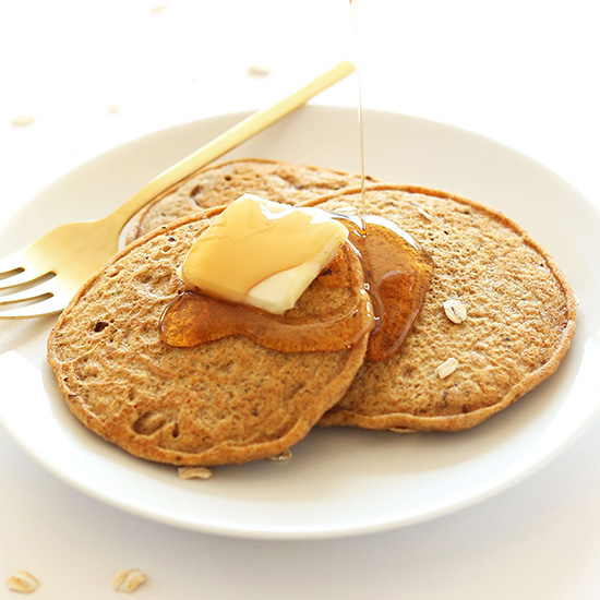 Drizzling syrup onto a plate of Vegan Whole Grain Pancakes