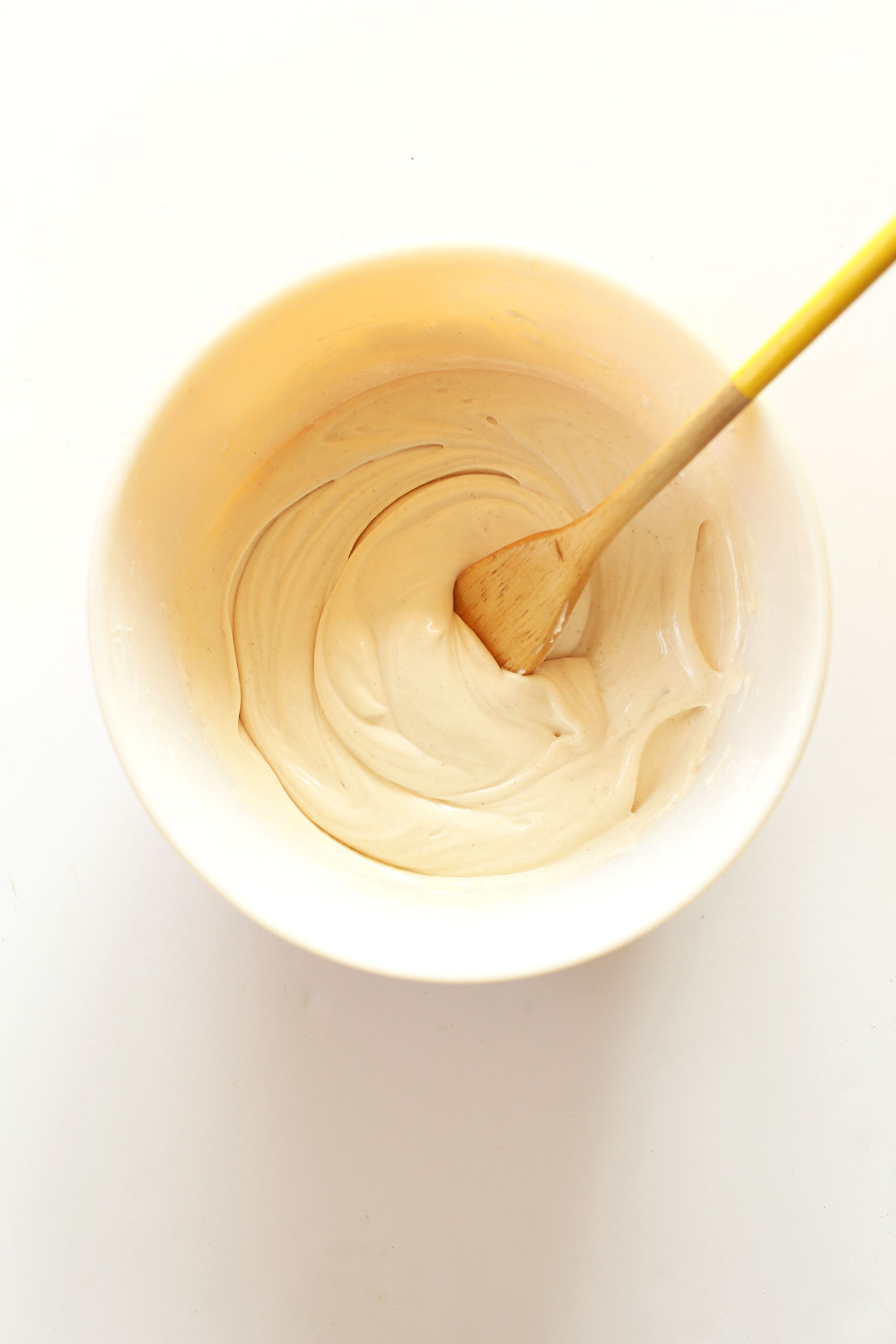 Using a wooden spoon to stir a bowl of our easy Vegan Cream Cheese Frosting