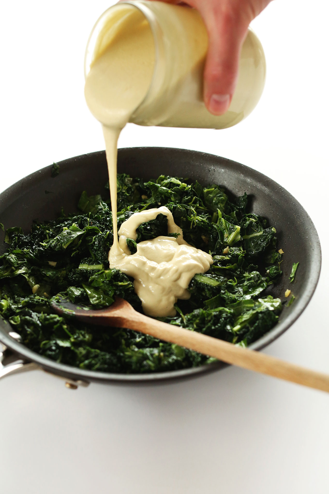 Pouring cashew sauce onto greens for healthy vegan Kale and Spinach Dip