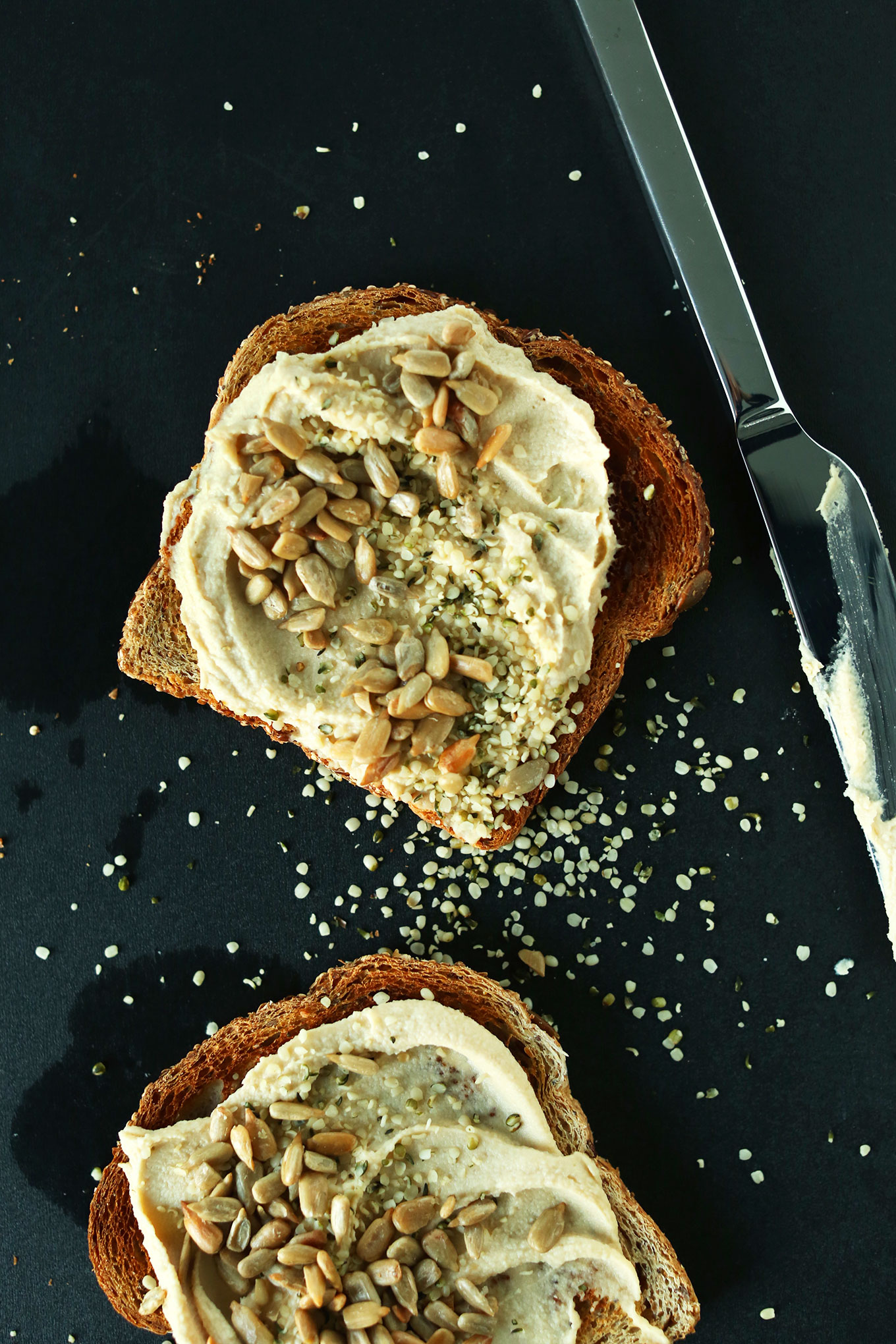 Slices of toast topped with hummus, hemp seeds, and sunflower seeds