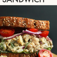 Vegan sandwich on a cutting board with text above it saying Vegan & Gluten-Free Chickpea Sunflower Sandwich