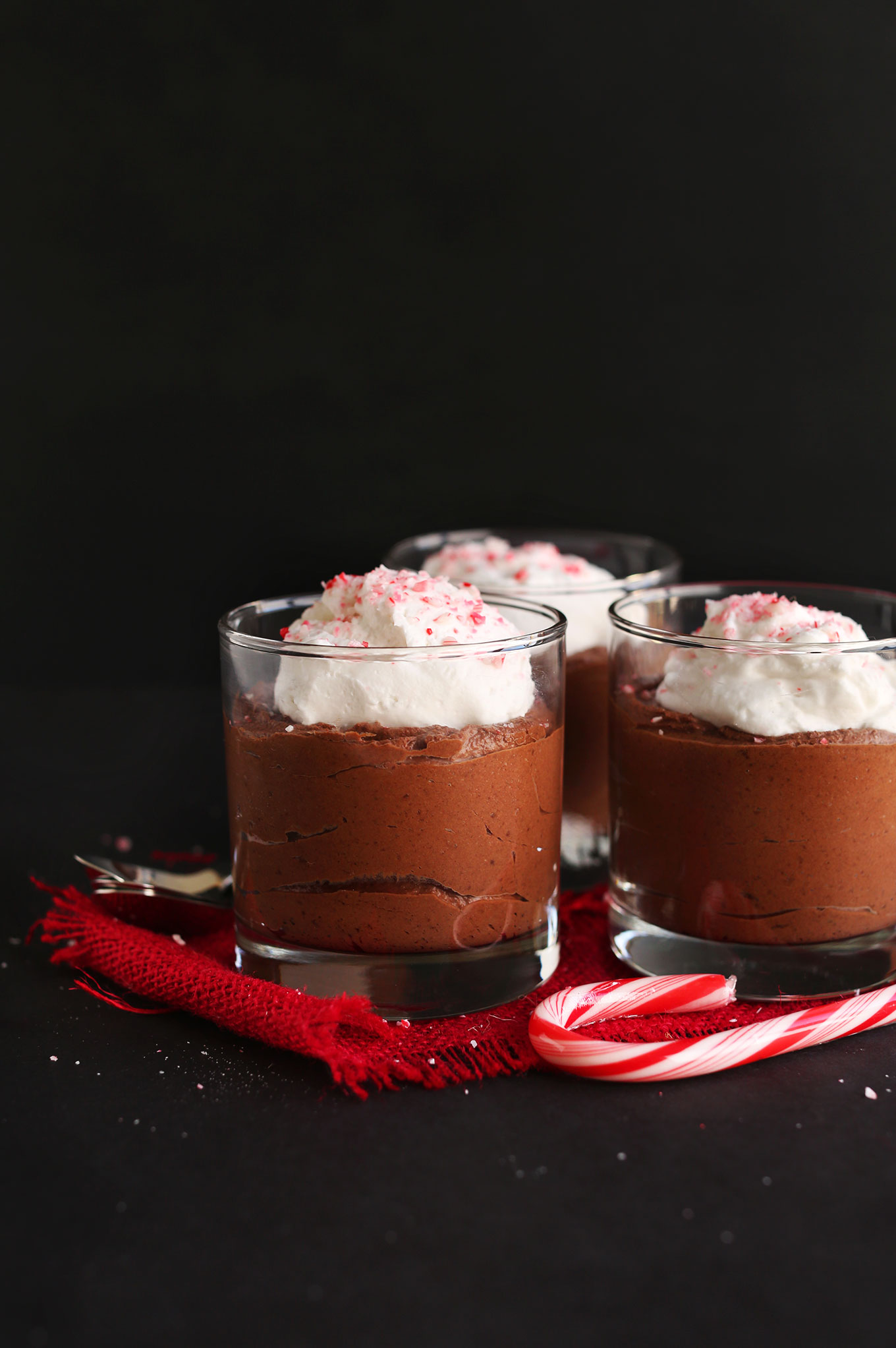 Jars of vegan Chocolate Peppermint Mousse topped with coconut whip and crushed candy cane