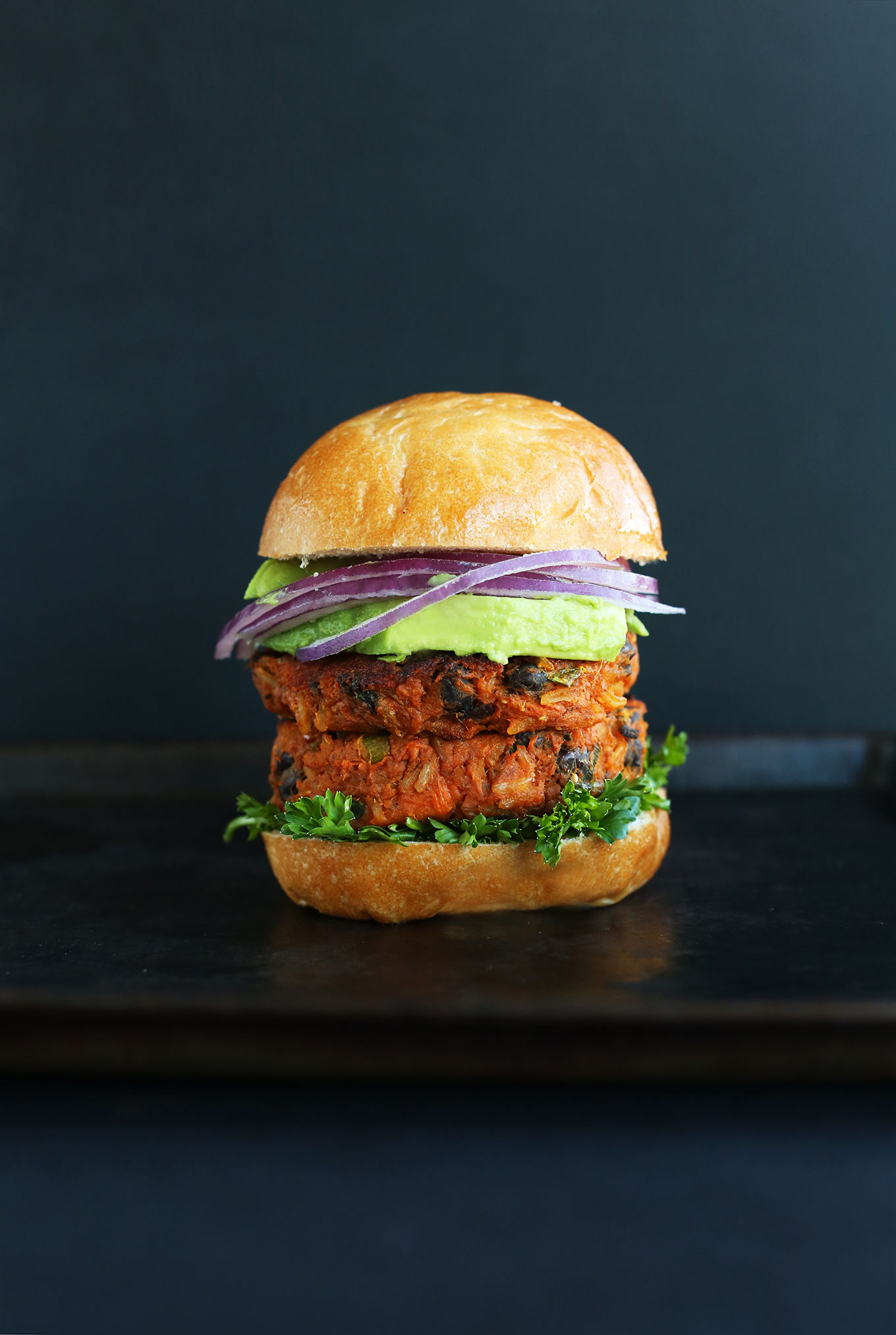 Sweet Potato Black Bean Burgers in a bun with parsley, avocado, and red onion on a bun