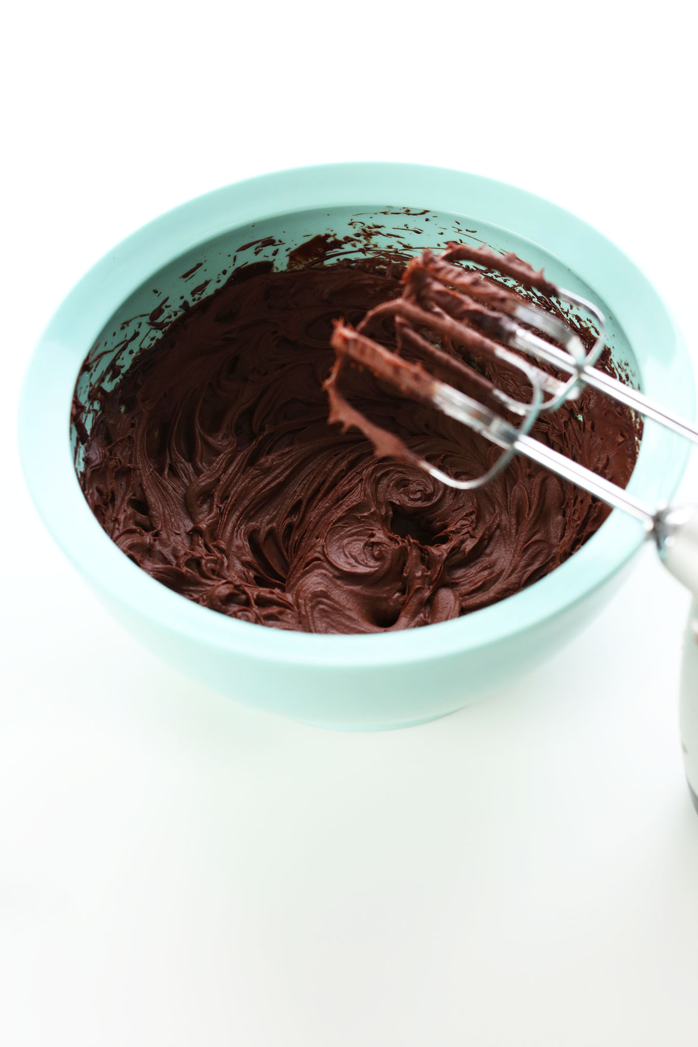 Electric mixer blades resting over a bowl of the Best Vegan Chocolate Ganache Frosting