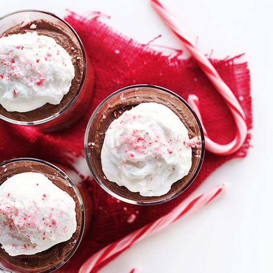 Three short glasses of Vegan Dark Chocolate Peppermint Mousse topped with coconut whipped cream and crushed candy cane