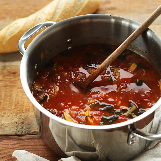 Drewniana łyżka w garnku z zupą pomidorowo-warzywną z białej fasoli