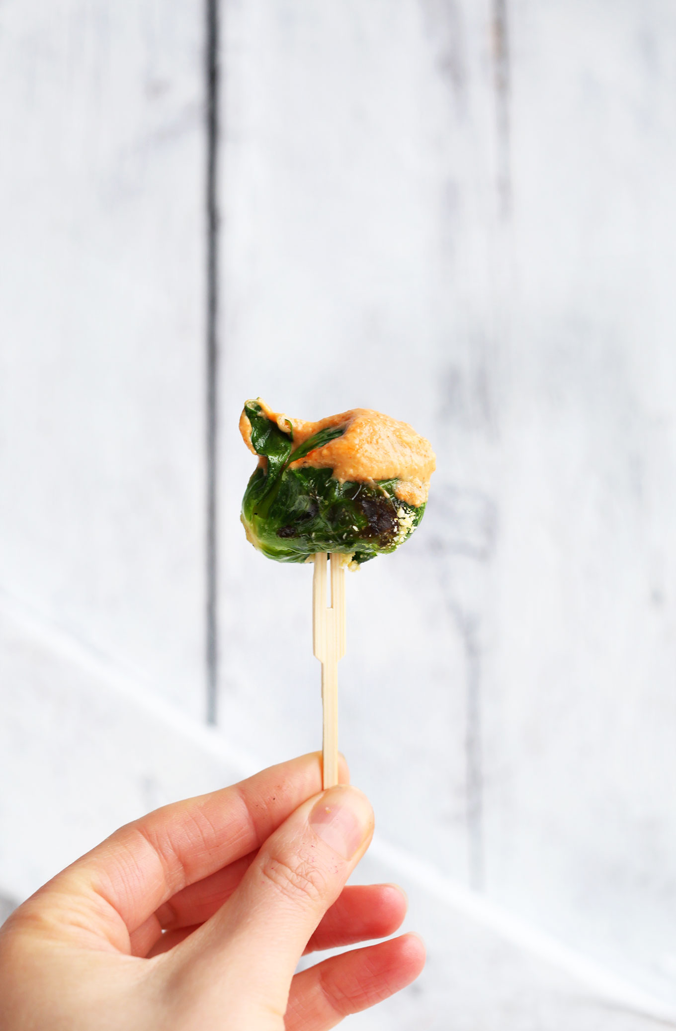 Toothpick holding up a Crispy Brussels Sprout topped with vegan Sriracha Aioli