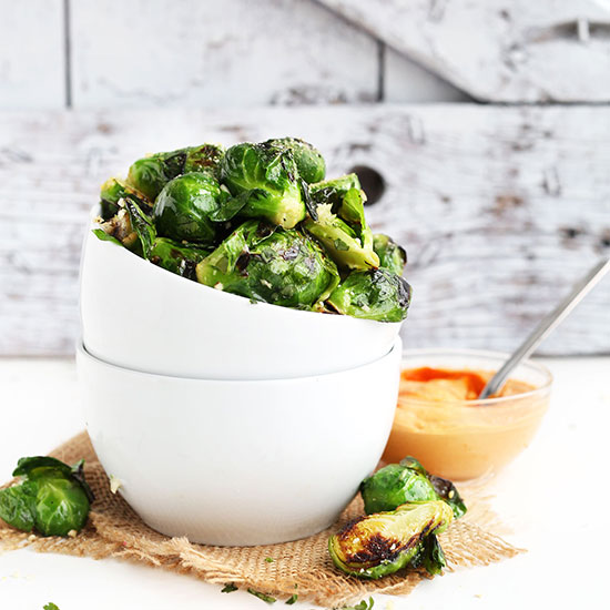 Bowl of Vegan Sriracha Aioli and stack of bowls filled with Crispy Roasted Brussels Sprouts