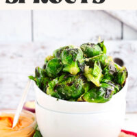 Bowl of crispy garlic Brussels sprouts next to a bowl of vegan sriracha aioli