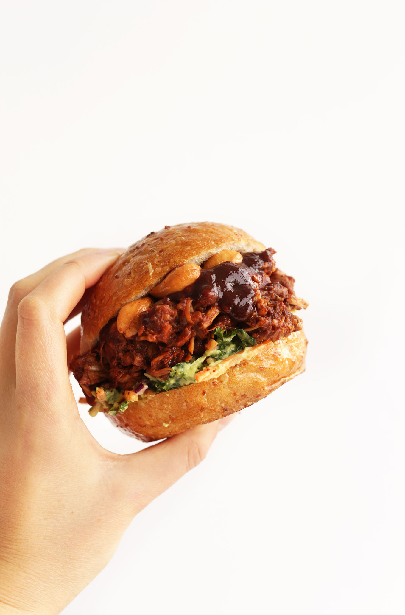 Holding up an amazing BBQ Jackfruit Sandwich topped with Avocado Slaw and Roasted Cashews