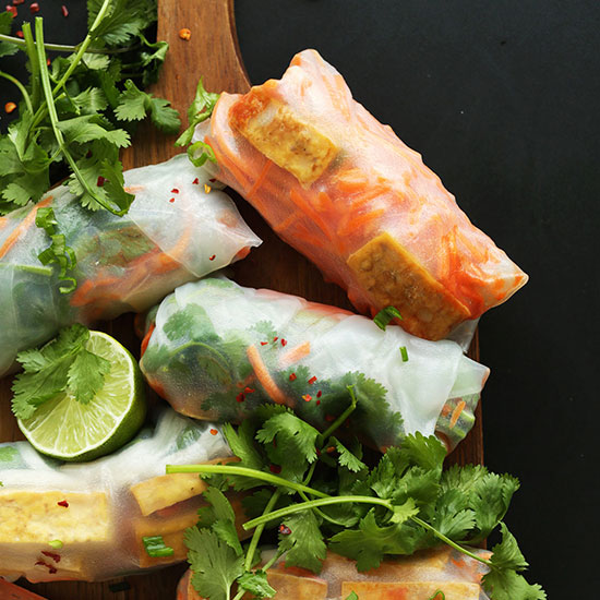 Several Banh Mi Spring Rolls on a cutting board with lime and fresh cilantro