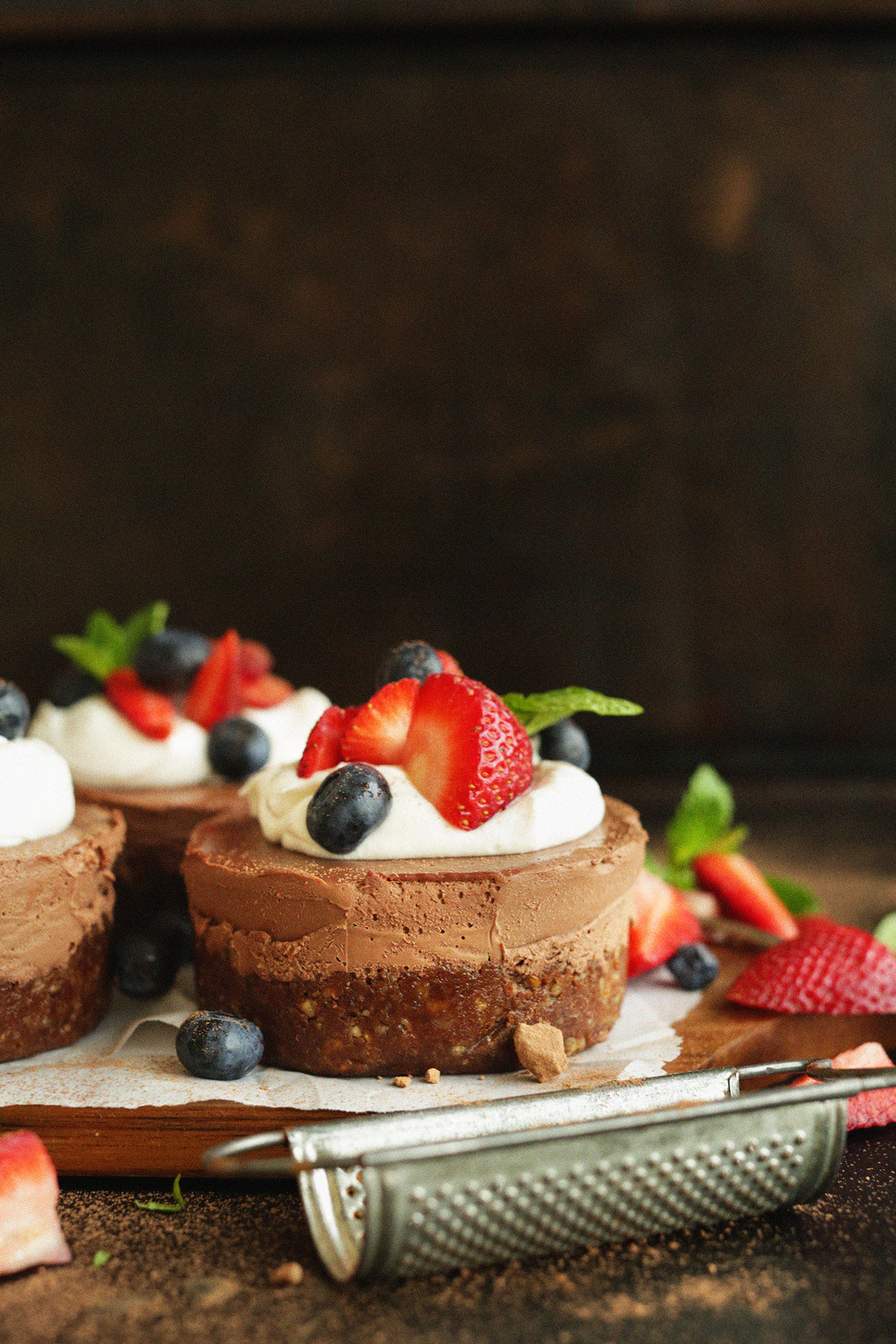 Cutting board with Mini Chocolate Cheesecakes topped with coconut whip and berries
