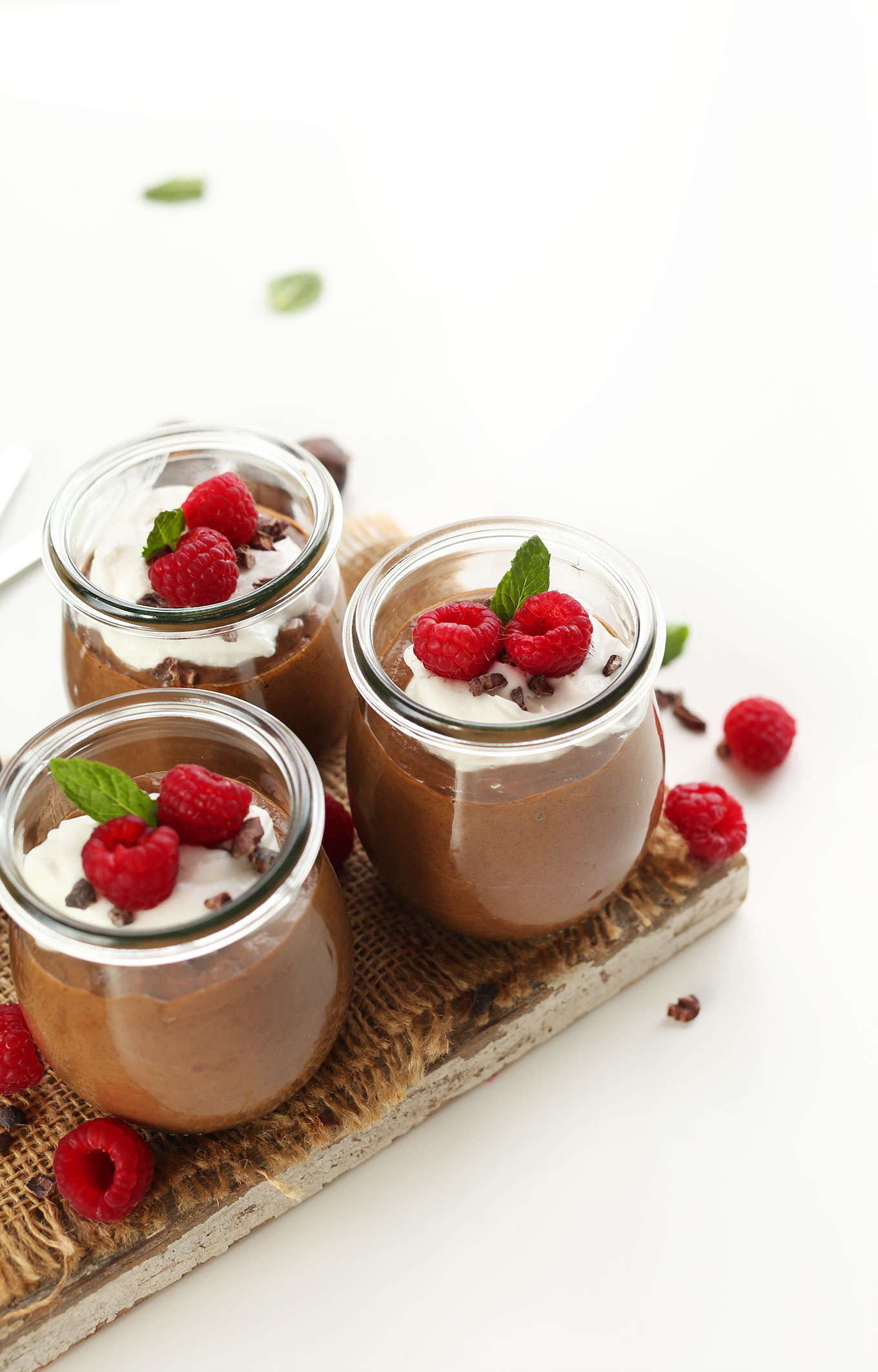 Jars of Chocolate Chia Seed Pudding topped with vegan coconut whip and fresh raspberries