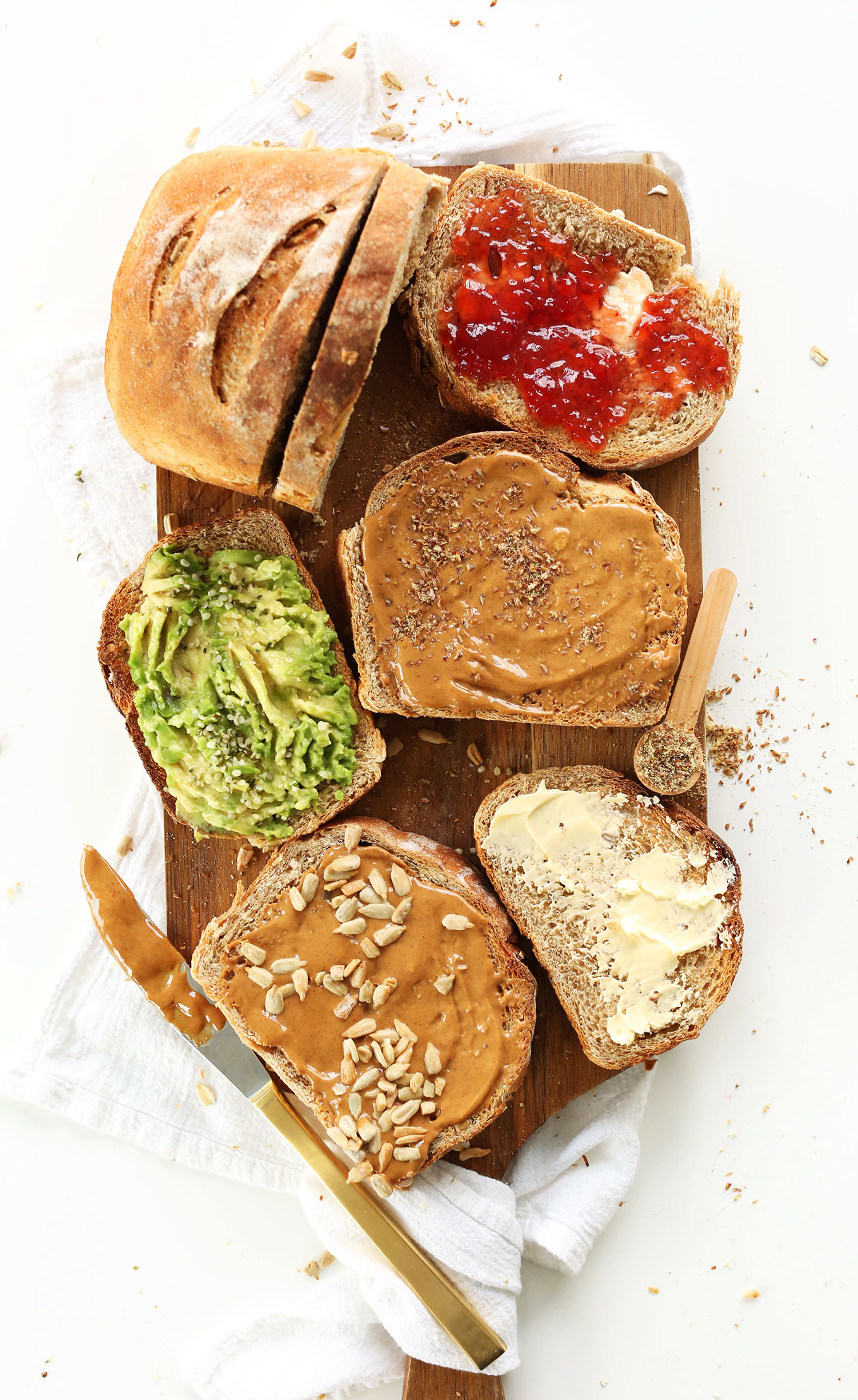 Slices of homemade bread with vegan butter, nut butter, avocado, and jam