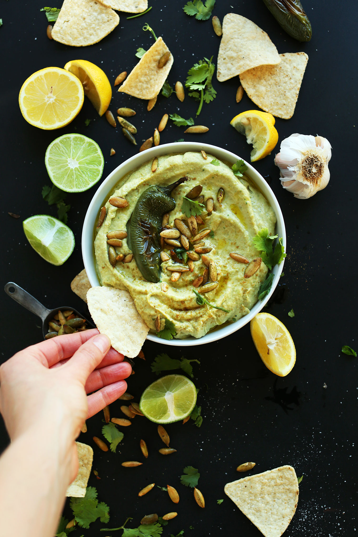 Dipping a tortilla chip into a bowl of our spicy Roasted Jalapeno Hummus recipe