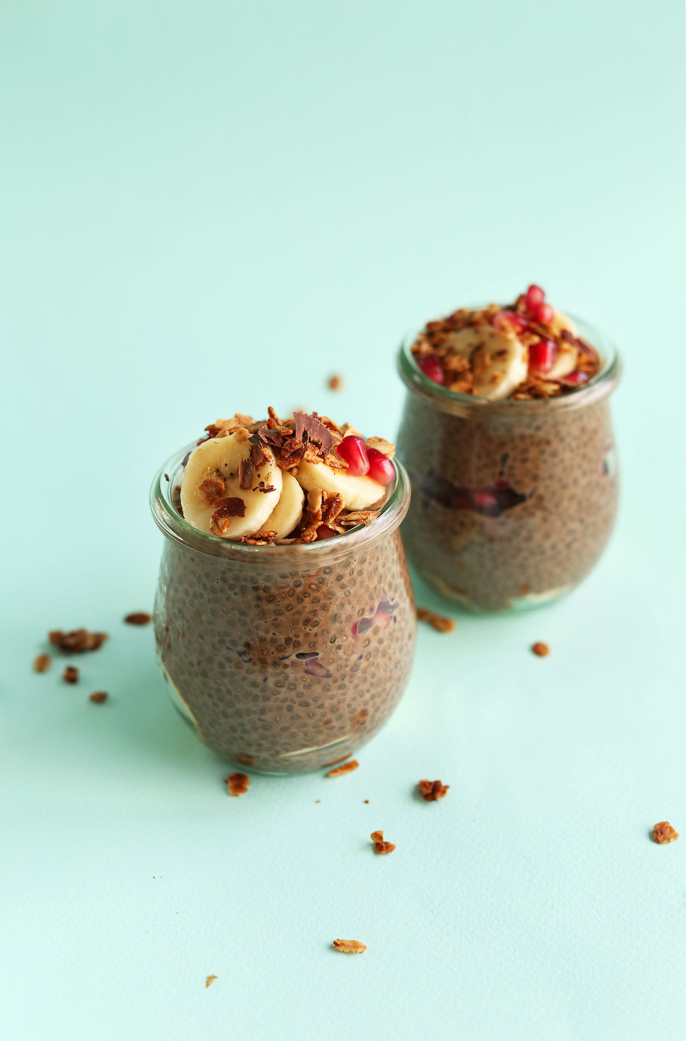 Jars of Chocolate Chia Seed Pudding topped with sliced bananas, cacao nibs, and pomegranate seeds