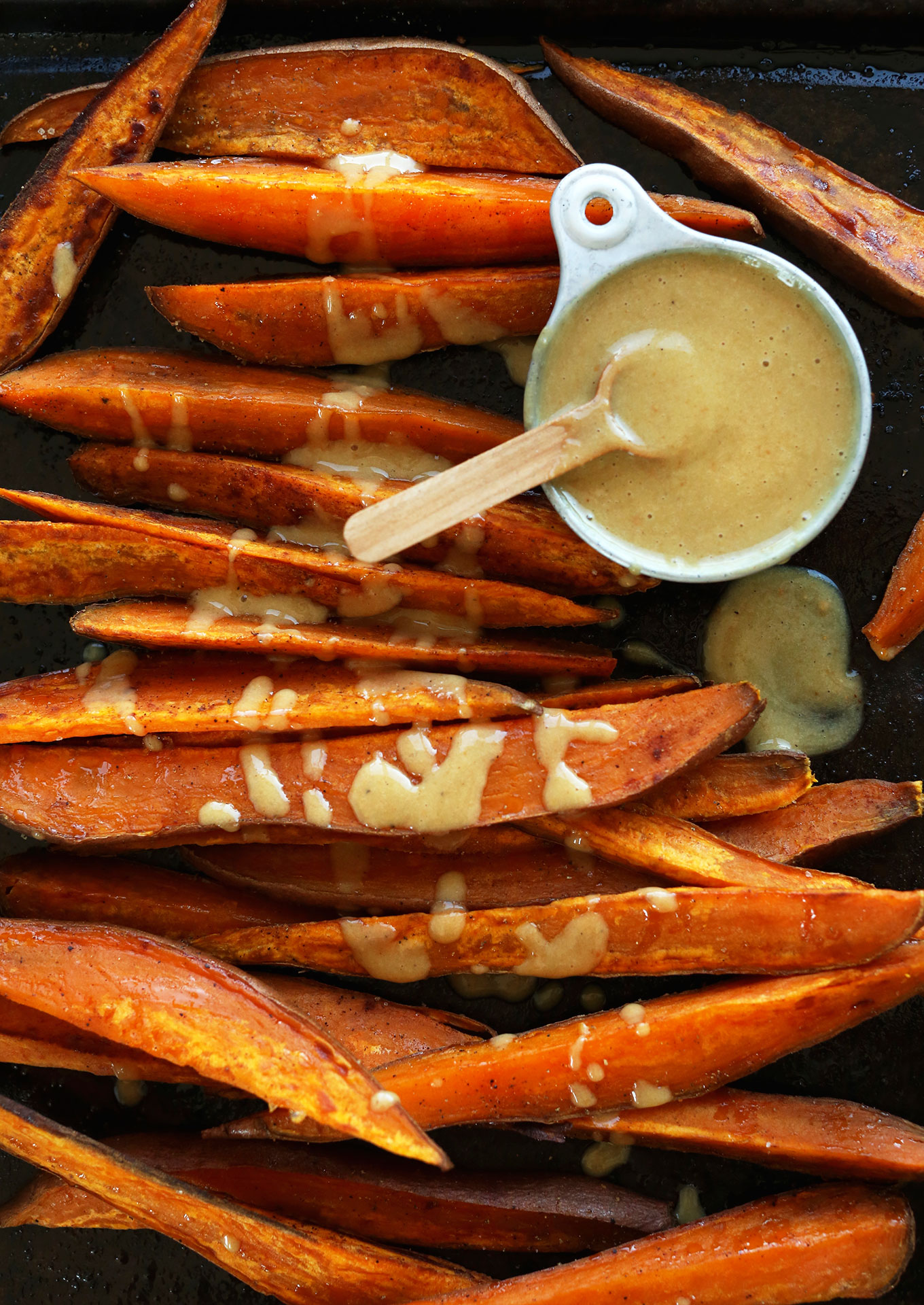 Baking sheet of Roasted Sweet Potato Wedges drizzled with No-Honey Mustard Dipping Sauce