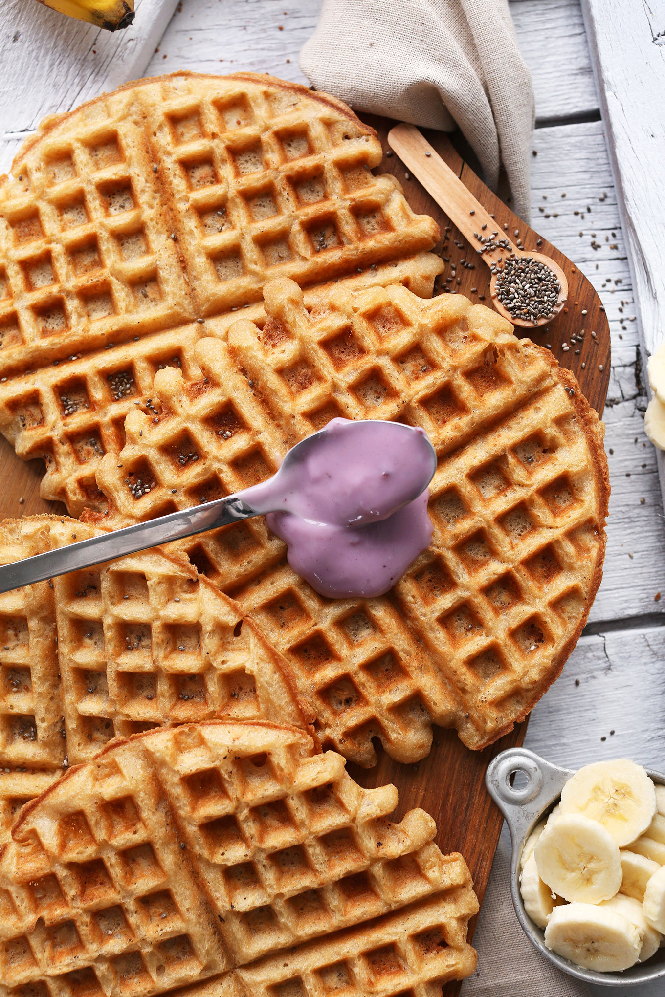 Pouring a spoonful of blueberry yogurt onto homemade gluten-free vegan waffles