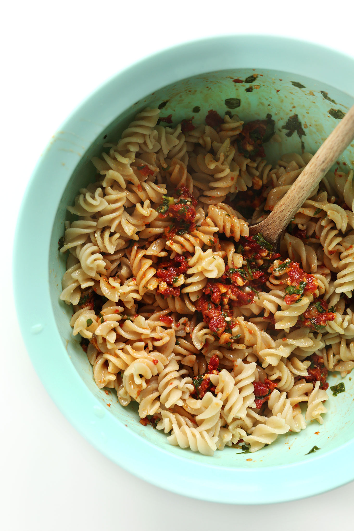 Mixing gluten-free noodles and vegan Sun-Dried Tomato Pesto in a mixing bowl