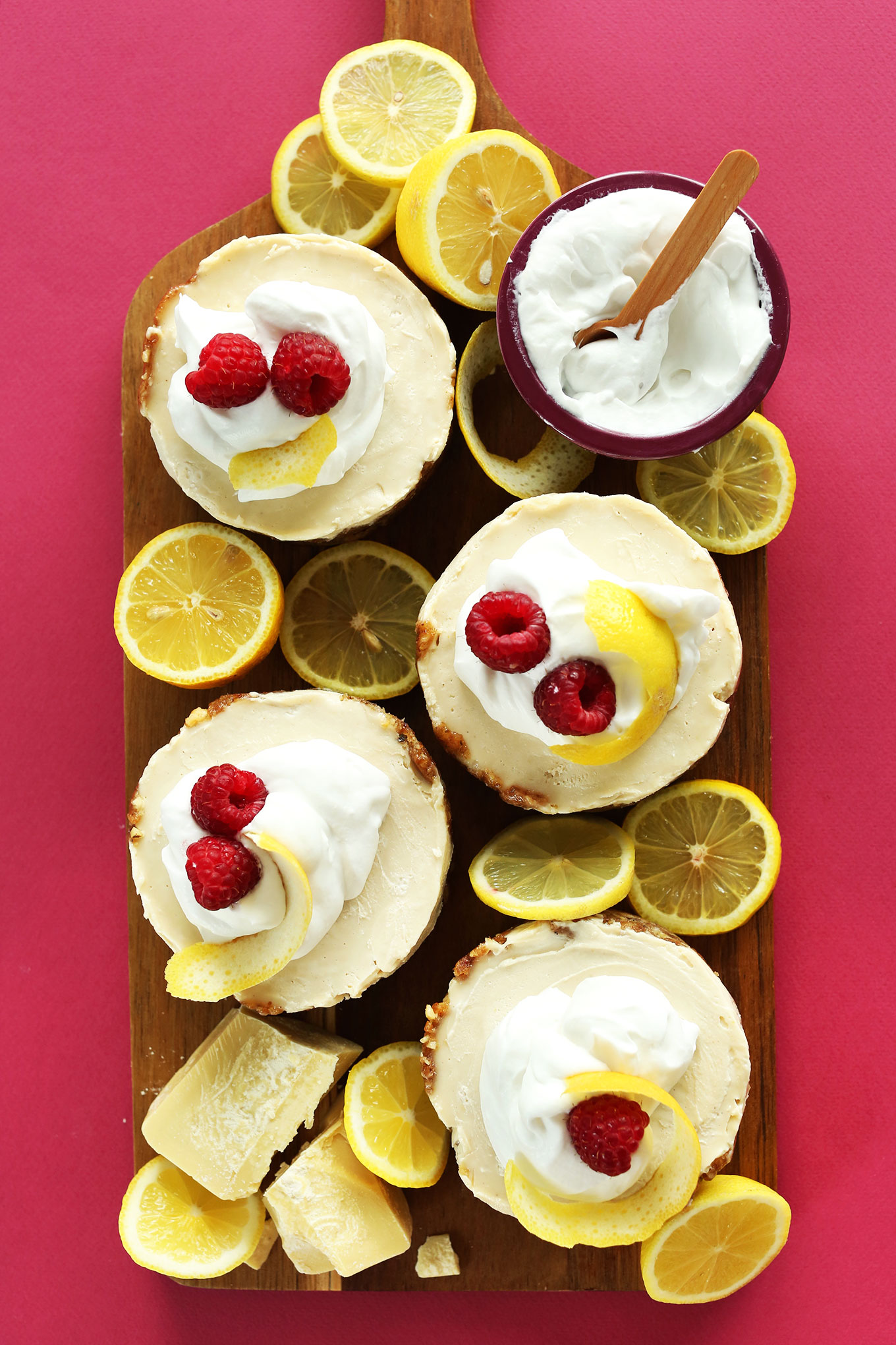 Lemon White Chocolate Cheesecakes topped with coconut whip, lemon rind, and fresh raspberries