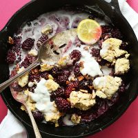 Skillet of homemade Blackberry Cobbler topped with coconut whipped cream and a lemon