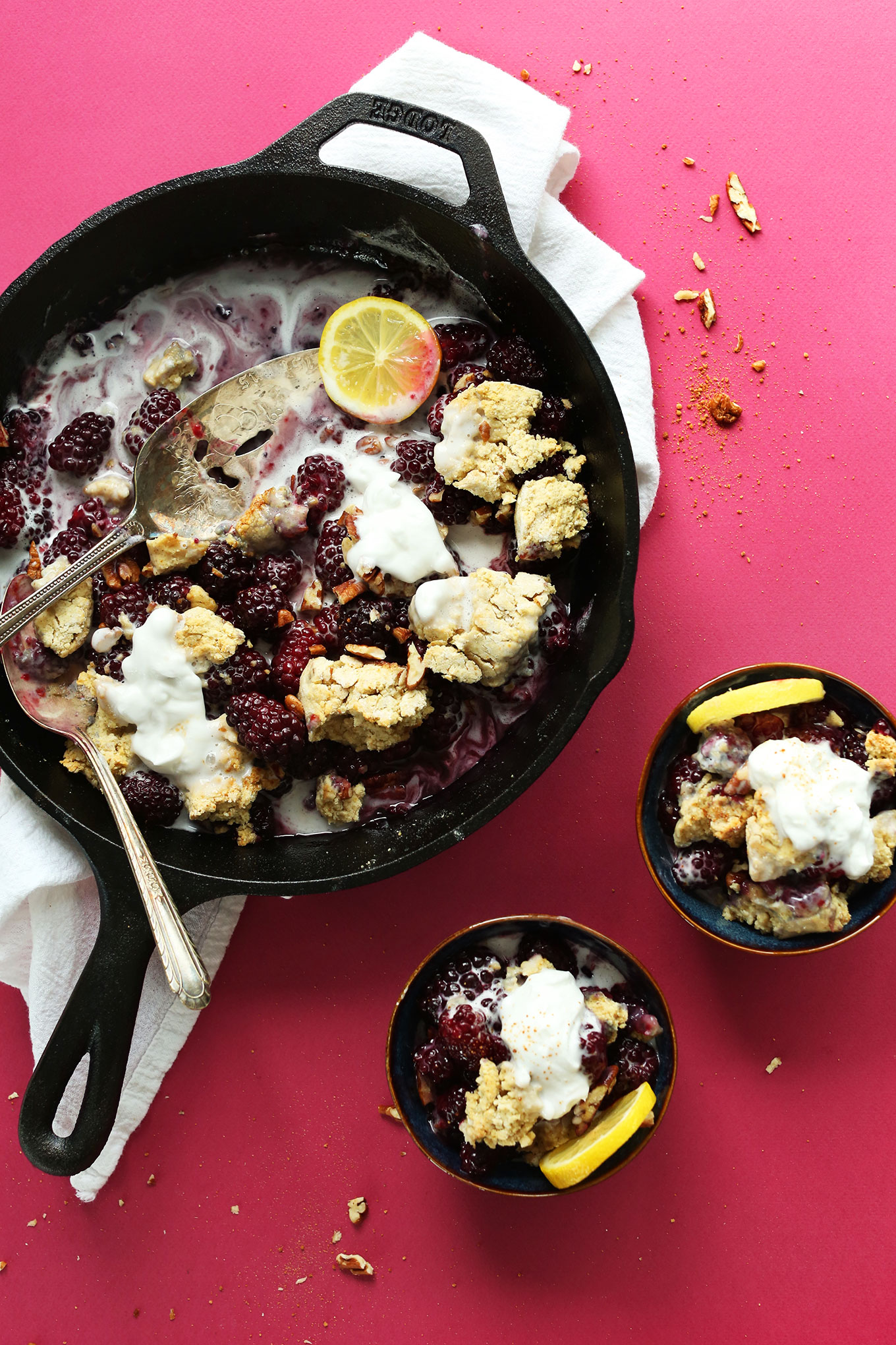 Dessert bowls and a cast-iron skillet filled with healthy Blackberry Cobbler topped with coconut whip