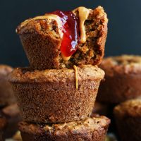 Stack of Vegan PB&J Muffins with the top one having a bite removed and jam and peanut butter dripping down it