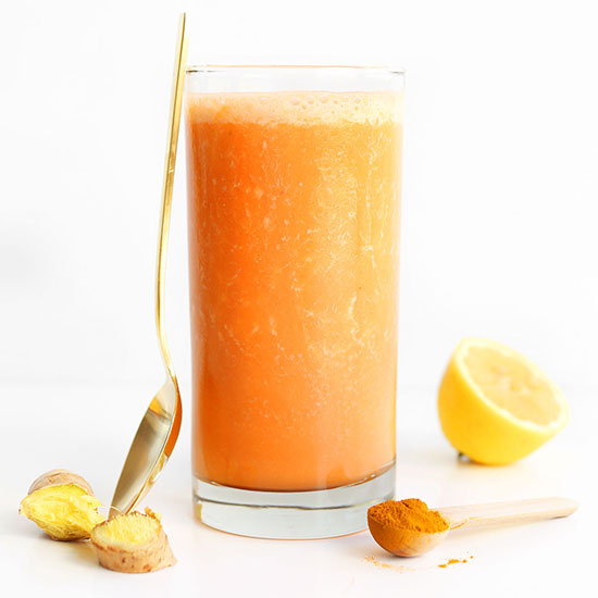 Gold spoon leaning against a glass of our Carrot Ginger Turmeric Smoothie recipe