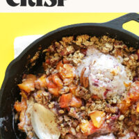 Servings spoons in a skillet of vegan gluten-free peach crisp topped with scoops of ice cream