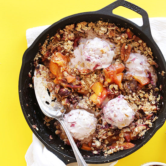 Cast-iron skillet filled with our Easy Peach Crisp recipe topped with scoops of ice cream