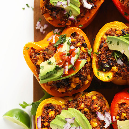 Cutting board of Spanish Quinoa Stuffed Peppers topped with avocado, cilantro, and onion