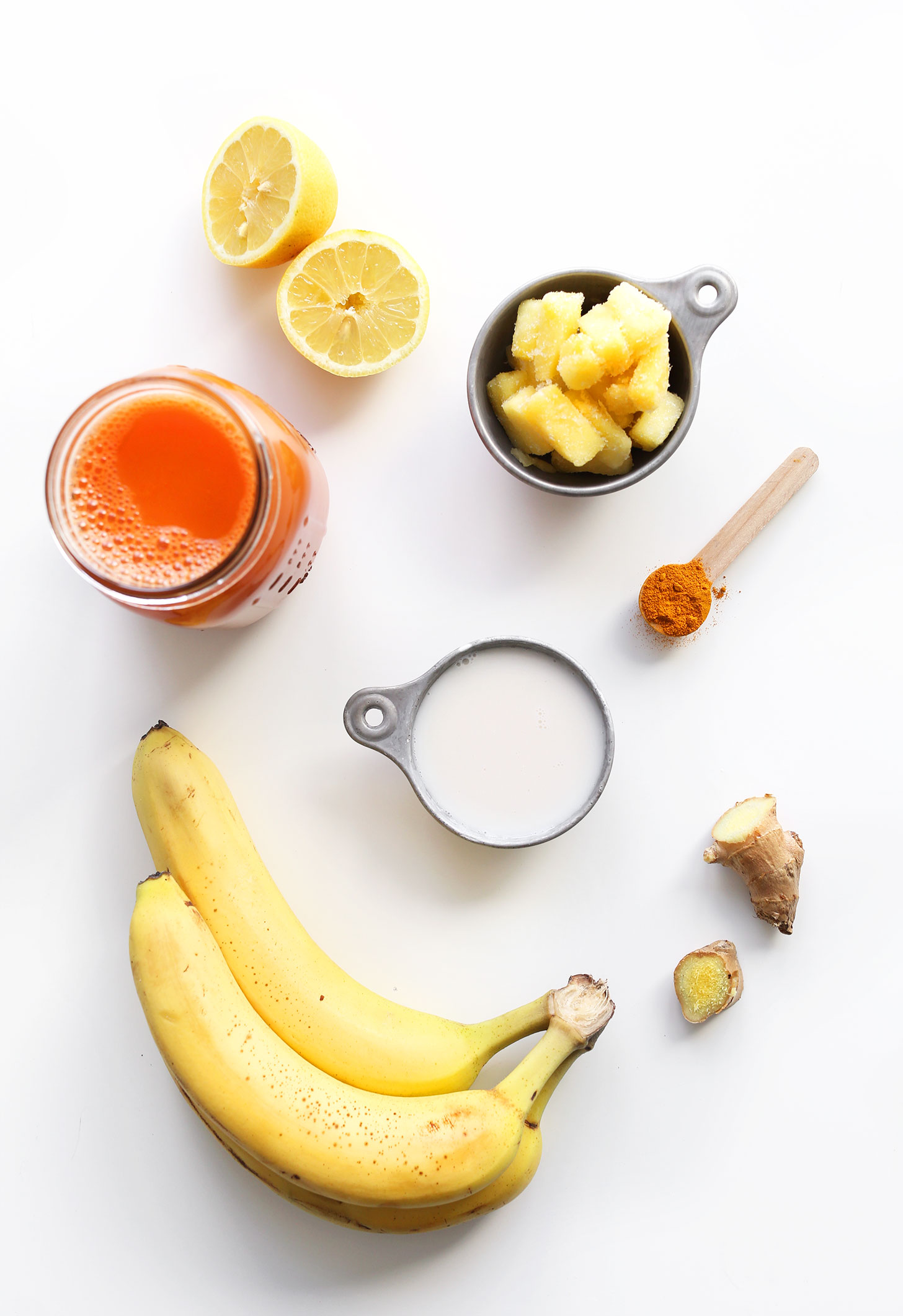 Bananas, ginger, turmeric, pineapple, lemon, carrot juice, and coconut milk for making a refreshing vegan smoothie