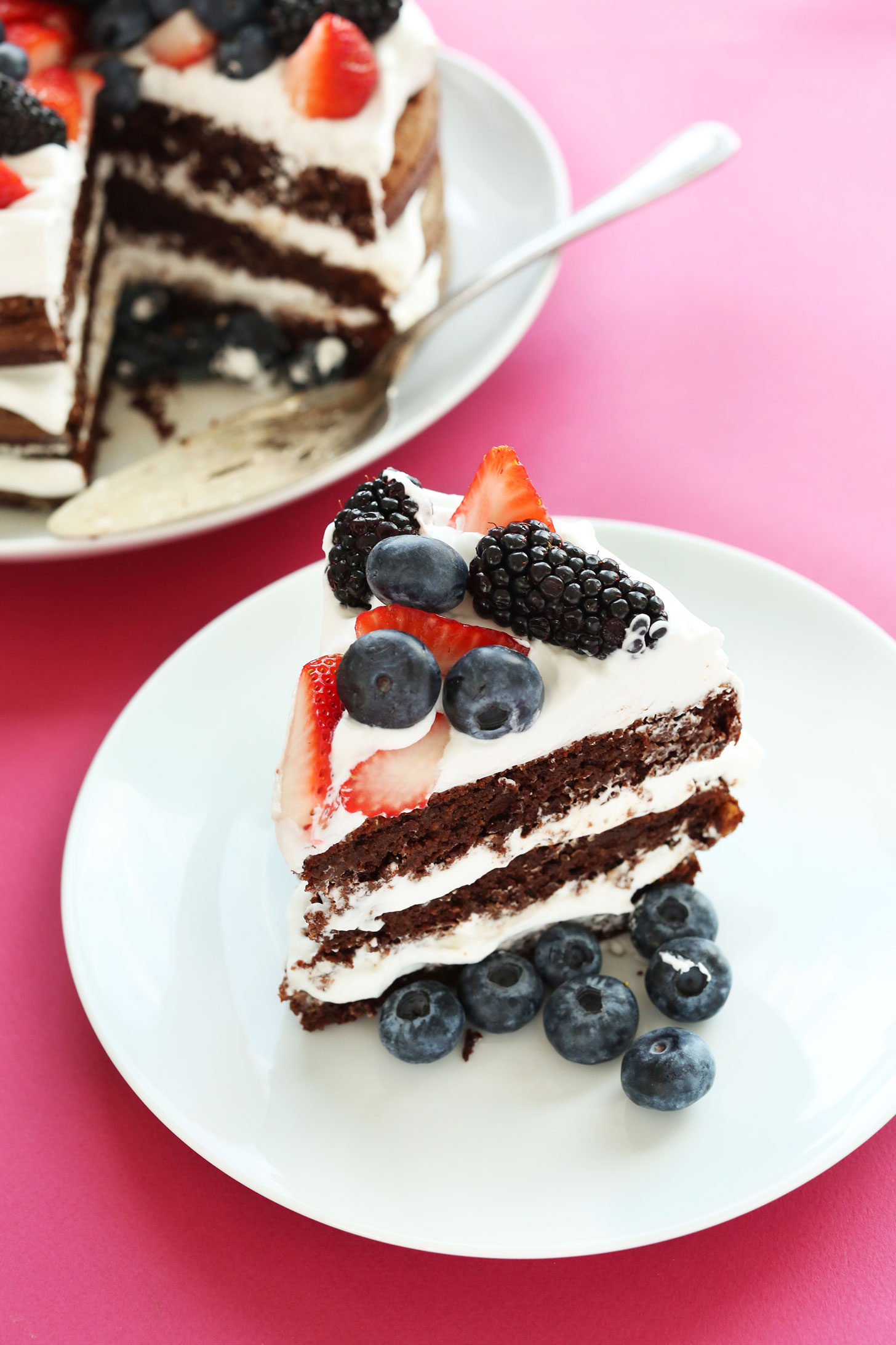 Slice of gluten-free vegan Chocolate Cake with Coconut Whipped Cream and fresh berries