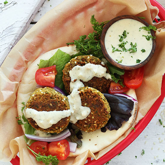Takeout basket filled with Easy Vegan Falafel on pita with vegetables and sauce