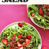 Two plates of strawberry arugula salad on a pink background